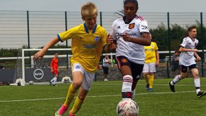 A boy in yellow Albion kit challenging for a football with a girl wearing Manchester United kit