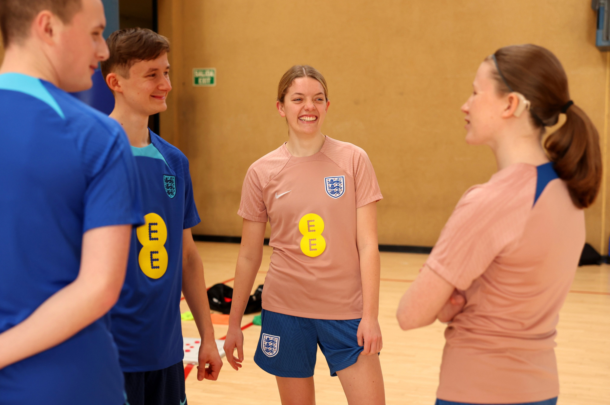 Jake and Faye, wearing England training kit, smile in a group discussion in a sports hall.